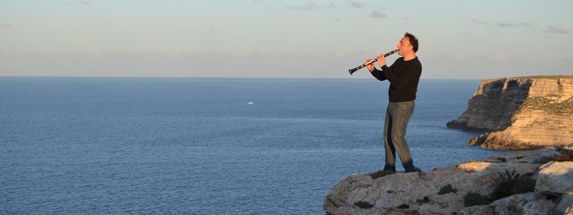 Vito Manzari suona il clarinetto su una scogliera, con il mare alle spalle